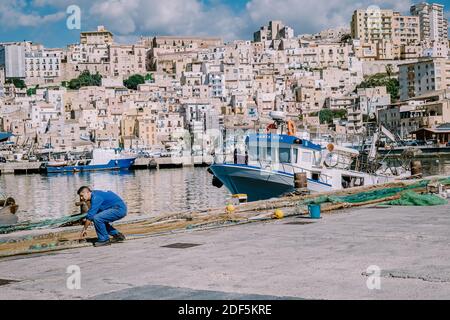 Sciacca Sizilien Oktober 2020, Fischerboote und Menschen reparieren Netze in der bunten Stadt Sciacca mit Blick auf ihren Hafen. Provinz Agrigento, Sizilien. Hochwertige Fotos Stockfoto