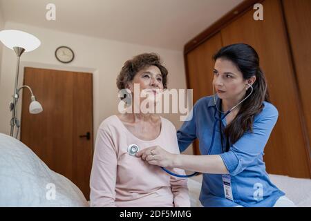 Niedrige Winkelansicht der Krankenschwester, die beim Herzen älterer weiblicher Patienten mit Stethoskop im Krankenhauszimmer zuhört. Stockfoto