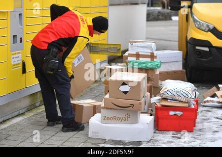München, Deutschland. Dezember 2020. Paketvolumen und Online-Handel boomen in Zeiten der Corona-Virus-Pandemie. DHL Paketzusteller, Paketdienstleister, bei der Arbeit legt Paket in ein Fach einer Packstation. Entlädt seine Paket Auto, Postbus, DHL, Paket, Pakete, Paketdienst, liefern, liefern, entladen, Versand, Transporter, Handfahrzeug. Quelle: dpa/Alamy Live News Stockfoto