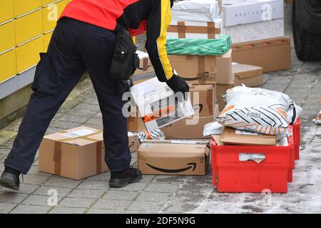 München, Deutschland. Dezember 2020. Paketvolumen und Online-Handel boomen in Zeiten der Corona-Virus-Pandemie. DHL Paketzusteller, Paketdienstleister, bei der Arbeit, entlädt seinen Paketwagen, Postbus, DHL, Paket, Pakete, Paketdienst, liefern, liefern, entladen, Versand, Transporter, Handfahrzeug. Quelle: dpa/Alamy Live News Stockfoto