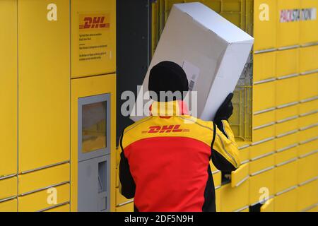 München, Deutschland. Dezember 2020. Paketvolumen und Online-Handel boomen in Zeiten der Corona-Virus-Pandemie. DHL Paketzusteller, Paketdienstleister, bei der Arbeit legt Paket in ein Fach einer Packstation. Entlädt seine Paket Auto, Postbus, DHL, Paket, Pakete, Paketdienst, liefern, liefern, entladen, Versand, Transporter, Handfahrzeug. Quelle: dpa/Alamy Live News Stockfoto