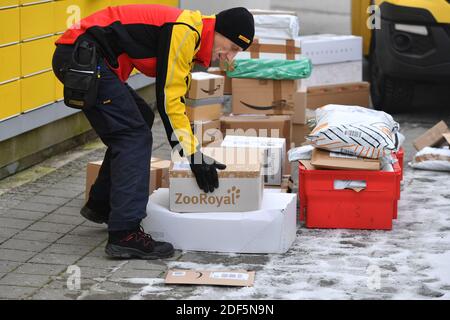 München, Deutschland. Dezember 2020. Paketvolumen und Online-Handel boomen in Zeiten der Corona-Virus-Pandemie. DHL Paketzusteller, Paketdienstleister, bei der Arbeit legt Paket in ein Fach einer Packstation. Entlädt seine Paket Auto, Postbus, DHL, Paket, Pakete, Paketdienst, liefern, liefern, entladen, Versand, Transporter, Handfahrzeug. Quelle: dpa/Alamy Live News Stockfoto