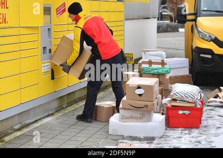 München, Deutschland. Dezember 2020. Paketvolumen und Online-Handel boomen in Zeiten der Corona-Virus-Pandemie. DHL Paketzusteller, Paketdienstleister, bei der Arbeit legt Paket in ein Fach einer Packstation. Entlädt seine Paket Auto, Postbus, DHL, Paket, Pakete, Paketdienst, liefern, liefern, entladen, Versand, Transporter, Handfahrzeug. Quelle: dpa/Alamy Live News Stockfoto