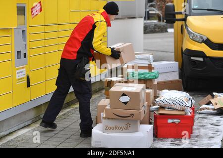 München, Deutschland. Dezember 2020. Paketvolumen und Online-Handel boomen in Zeiten der Corona-Virus-Pandemie. DHL Paketzusteller, Paketdienstleister, bei der Arbeit legt Paket in ein Fach einer Packstation. Entlädt seine Paket Auto, Postbus, DHL, Paket, Pakete, Paketdienst, liefern, liefern, entladen, Versand, Transporter, Handfahrzeug. Quelle: dpa/Alamy Live News Stockfoto