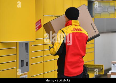 München, Deutschland. Dezember 2020. Paketvolumen und Online-Handel boomen in Zeiten der Corona-Virus-Pandemie. DHL Paketzusteller, Paketdienstleister, bei der Arbeit legt Paket in ein Fach einer Packstation. Entlädt seine Paket Auto, Postbus, DHL, Paket, Pakete, Paketdienst, liefern, liefern, entladen, Versand, Transporter, Handfahrzeug. Quelle: dpa/Alamy Live News Stockfoto
