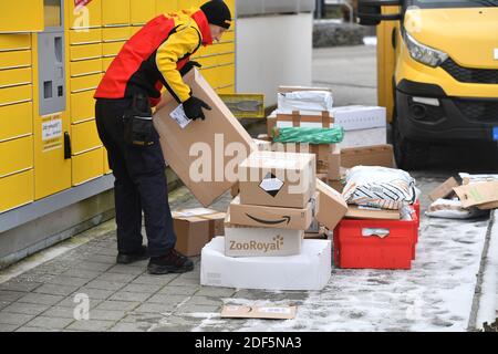München, Deutschland. Dezember 2020. Paketvolumen und Online-Handel boomen in Zeiten der Corona-Virus-Pandemie. DHL Paketzusteller, Paketdienstleister, bei der Arbeit legt Paket in ein Fach einer Packstation. Entlädt seine Paket Auto, Postbus, DHL, Paket, Pakete, Paketdienst, liefern, liefern, entladen, Versand, Transporter, Handfahrzeug. Quelle: dpa/Alamy Live News Stockfoto