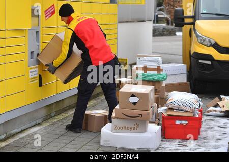 München, Deutschland. Dezember 2020. Paketvolumen und Online-Handel boomen in Zeiten der Corona-Virus-Pandemie. DHL Paketzusteller, Paketdienstleister, bei der Arbeit legt Paket in ein Fach einer Packstation. Entlädt seine Paket Auto, Postbus, DHL, Paket, Pakete, Paketdienst, liefern, liefern, entladen, Versand, Transporter, Handfahrzeug. Quelle: dpa/Alamy Live News Stockfoto