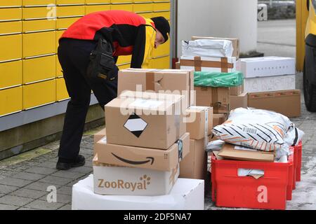 München, Deutschland. Dezember 2020. Paketvolumen und Online-Handel boomen in Zeiten der Corona-Virus-Pandemie. DHL Paketzusteller, Paketdienstleister, bei der Arbeit legt Paket in ein Fach einer Packstation. Entlädt seine Paket Auto, Postbus, DHL, Paket, Pakete, Paketdienst, liefern, liefern, entladen, Versand, Transporter, Handfahrzeug. Quelle: dpa/Alamy Live News Stockfoto