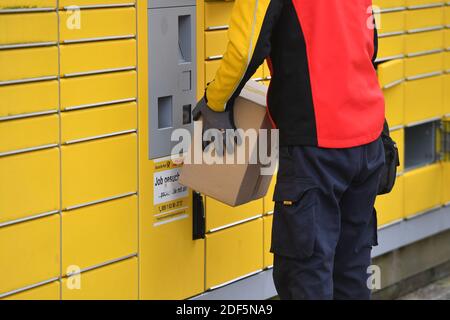 München, Deutschland. Dezember 2020. Paketvolumen und Online-Handel boomen in Zeiten der Corona-Virus-Pandemie. DHL Paketzusteller, Paketdienstleister, bei der Arbeit legt Paket in ein Fach einer Packstation. Entlädt seine Paket Auto, Postbus, DHL, Paket, Pakete, Paketdienst, liefern, liefern, entladen, Versand, Transporter, Handfahrzeug. Quelle: dpa/Alamy Live News Stockfoto