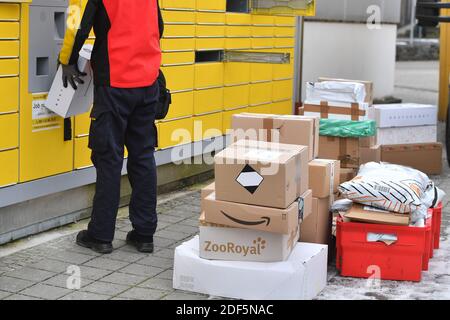 München, Deutschland. Dezember 2020. Paketvolumen und Online-Handel boomen in Zeiten der Corona-Virus-Pandemie. DHL Paketzusteller, Paketdienstleister, bei der Arbeit legt Paket in ein Fach einer Packstation. Entlädt seine Paket Auto, Postbus, DHL, Paket, Pakete, Paketdienst, liefern, liefern, entladen, Versand, Transporter, Handfahrzeug. Quelle: dpa/Alamy Live News Stockfoto