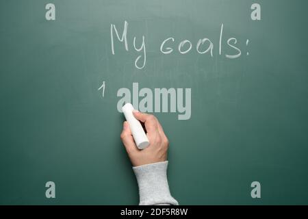 Hand hält ein weißes Stück Kreide auf dem Hintergrund einer Kreidetafel mit der Aufschrift mein Ziel, copy space Stockfoto