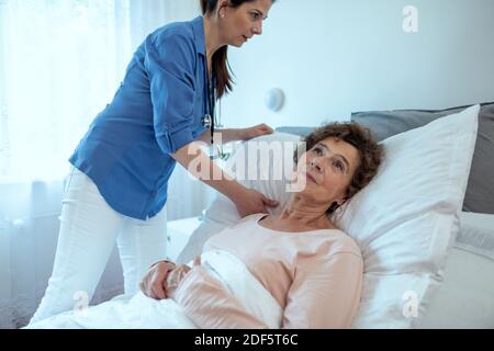 Home Caregiver Anpassung Kissen Für Ältere Weibliche Patienten. Krankenschwester, die sich um einen älteren Patienten im Krankenhausbett kümmern. Stockfoto