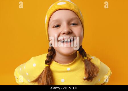 Lustige niedliche kleine Mädchen in einem Hut und mit Zöpfen auf einem gelben Hintergrund. Stockfoto