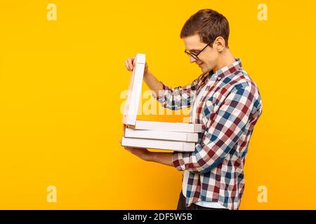 Ein Mann hält eine Schachtel Pizza auf einem gelben Hintergrund, ein Mann schaut in eine Schachtel Pizza Stockfoto