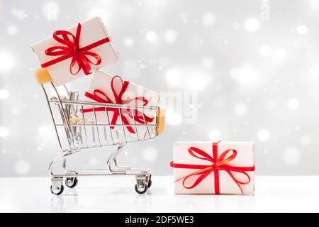 Weihnachtseinkäufe. Mini-Wagen mit Geschenken auf weißem Hintergrund mit Lichtern. Stockfoto