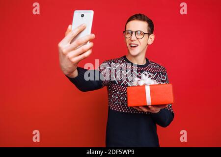 Ein Mann in einer Brille, mit einem Geschenk in den Händen, fotografiert sich selbst auf einem Smartphone Stockfoto