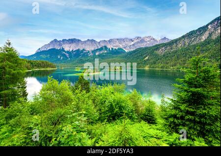 Kleine Inseln mit Kiefern mitten im Eibsee mit Zugspitze. Wunderschöne Landschaft mit paradiesischen Strand und klarem blauen Wat Stockfoto