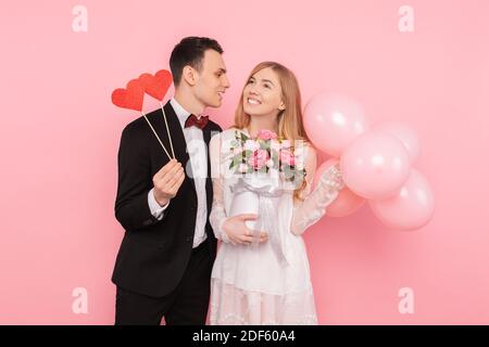 Ein liebevolles Paar, ein Mann hält zwei Papierherzen, und eine Frau hält einen Blumenstrauß und Ballons Stockfoto