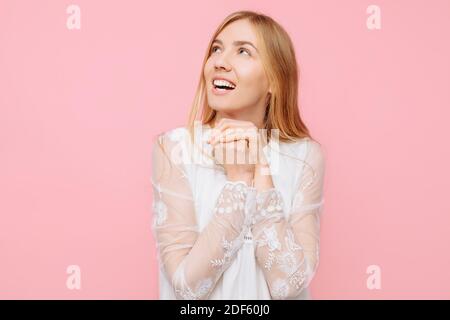 Glücklich enthusiastisches Mädchen in einem weißen Kleid, träumt von etwas, macht Pläne, und Blick auf einen leeren Raum im Hintergrund, auf einem rosa Hintergrund Stockfoto