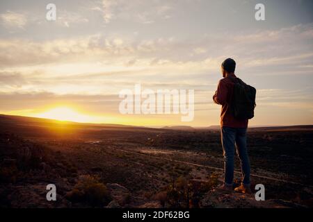 Low-Angle-Ansicht des jungen männlichen Wanderer mit Rucksack stehen Auf der Bergspitze beim Wandern mit Blick auf den Sonnenaufgang Stockfoto
