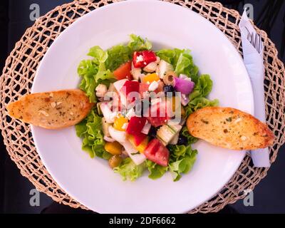 Weißer Teller mit griechischem Salat und zwei Scheiben Knoblauchbrot. Stockfoto
