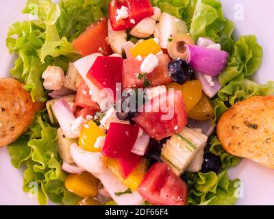 Weißer Teller mit griechischem Salat und zwei Scheiben Knoblauchbrot. Stockfoto