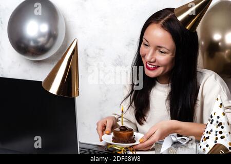 Online-Feier Konzept lächelnde junge Frau feiert Geburtstag halten Cupcake Mit Kerze und Videoanruf mit einem Freund in Quarantäne Zeit Stockfoto