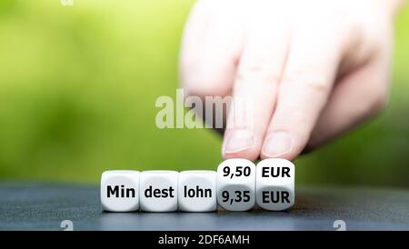 Hand dreht Würfel und ändert den deutschen Ausdruck 'Mindestlohn 9.30 EUR' in 'Mindestlohn 9.50 EUR' (Mindestlohn 9.50 EUR). Stockfoto