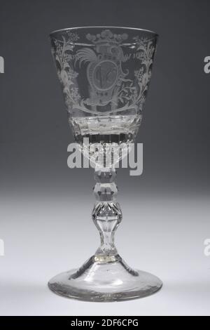 Glas, 3. Viertel 18. Jahrhundert, Allgemein: 20.2 x 9.3cm 202 x 93mm, Kelchdurchmesser: 8,8cm, Kartusche, V.O.C. Glas aus farblosen Glas. Der Kelch hat eine ziemlich hohe gewölbte Basis mit einem facettierten Fußring. Facettierter Stiel mit drei Knöpfen, dessen Boden balusterförmig ist. Eine gedehnte Luftblase im gesamten Stängel. In dem sehr massiven, facettierten Kelchboden, sechs Luftblasen: Eine in der Mitte, fünf um sie herum. An der Kelchwand wurde eine mit einer Grabkrone überzogene Rokokartusche, die von zwei blühenden Zweigen umgeben ist, mit dem Monogramm OVC [in einem], gebohrt Stockfoto