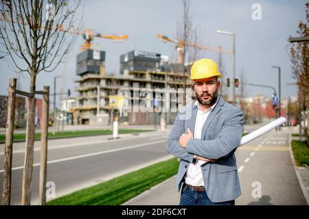 Porträt des bärtigen Architekten, der das Projekt auf der Baustelle hält. Stockfoto
