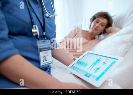 Digitales Tablet mit Testergebnissen älterer weiblicher Patientin, die im Bett im Hintergrund liegt. Nahaufnahme des digitalen Tablets mit Software für das Gesundheitswesen. Stockfoto