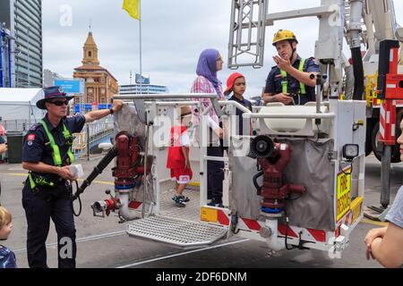 Mitglieder der neuseeländischen Feuerwehr demonstrieren einen Feuerwehrwagen Hydraulische Hebebühne zu einer Familiengruppe Stockfoto