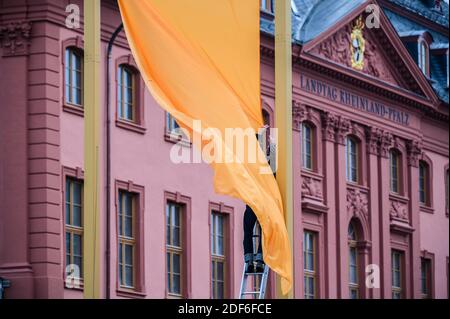 Mainz, Deutschland. Dezember 2020. Ein Mitarbeiter der Firma, die das Kunstwerk "drei Farben" gebaut hat, steht auf einer Leiter an einer der drei Flaggen. Vor der Baustelle des landtags wurde ein Testlauf durchgeführt, um die tatsächliche Wirkung des Kunstwerks zu beurteilen. Der Entwurf eines Berliner Künstlers mit dem Titel "drei Farben" wurde mit großer Mehrheit zum Gewinner des Wettbewerbs "Kunst am Bauen" gewählt. Das Kunstwerk basiert auf dem Hambacher Festival. Quelle: Andreas Arnold/dpa/Alamy Live News Stockfoto