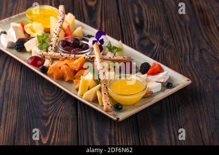 Käseplatte mit Trauben und Nüssen serviert. Verschiedene Käsesorten Camembert, Brie, Parmesan Blauschimmelkäse, Ziege mit Trauben, Gressini-Sticks, Cashews, Honig und Stockfoto