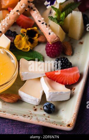 Käseplatte mit Trauben und Nüssen serviert. Verschiedene Käsesorten Camembert, Brie, Parmesan Blauschimmelkäse, Ziege mit Trauben, Gressini-Sticks, Cashews, Honig und Stockfoto