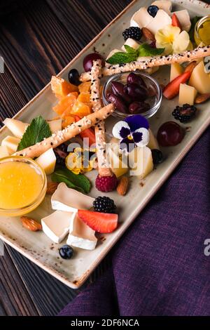 Käseplatte mit Trauben und Nüssen serviert. Verschiedene Käsesorten Camembert, Brie, Parmesan Blauschimmelkäse, Ziege mit Trauben, Gressini-Sticks, Cashews, Honig und Stockfoto