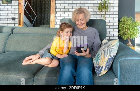 Großmutter und Enkelin verbringen Zeit miteinander und lesen Märchen und Geschichten auf einem E-Book oder Tablet. Herzliche Familienbeziehung. Pflege von g Stockfoto