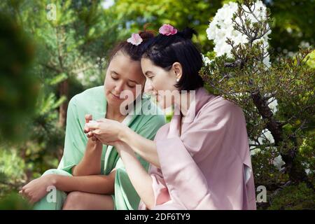 Japanischer Garten. Zwei junge schöne Frauen in japanischem Kimono im Garten, die die Schönheit des japanischen Gartens und blühende Blumen genießen Stockfoto