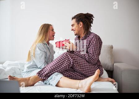 Fröhlicher Mann, der glückliche Freundin im Schlafzimmer ein Geschenk macht Stockfoto