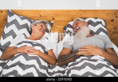 Glückliches Seniorenpaar lächelt zusammen im Bett - Hipster reif Leute, die eine lustige Schlafzeit haben - älterer Lebensstil und Liebe Beziehungskonzept Stockfoto