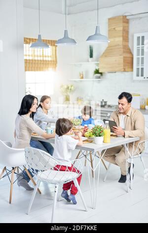 In voller Länge Aufnahme von fröhlichen hispanischen Familie genießen Mahlzeit zusammen beim Mittagessen, sitzen am Tisch in der Küche zu Hause. Kindheit, Essen Konzept Stockfoto