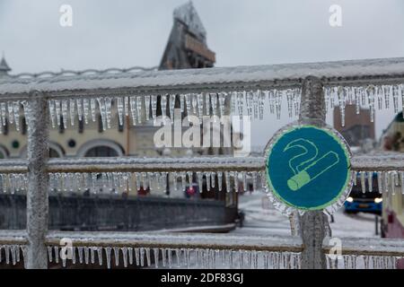 Rauchfreies Schild, das an verchromten, Stahlgeländern in der Stadt hängt. Die Geländer sind sehr eisig, Eiszapfen hängen. Stockfoto