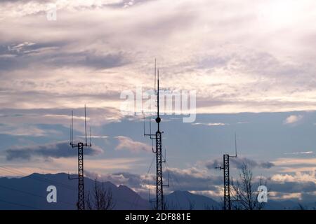 Drei Telekommunikationsmasten oder mobile Türme mit Satellitenantennen Silhouetten bei Sonnenuntergang cludy Himmel Hintergrund. Stockfoto