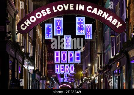 London, Großbritannien. - 2 Dez 2020: Die Carnaby Street 2020 Weihnachtsbeleuchtung, in diesem Jahr in Partnerschaft mit Charity Choose Love, die eine Reihe von Leuchtkästen mit positiven Botschaften sieht. Stockfoto