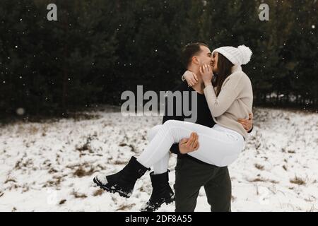 Mann hält Frau in den Händen und küsst sie im Winterwald. Ort für Ihren Text. Liebe, Beziehung, Winterurlaub. Stockfoto