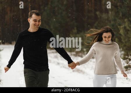 Lächelndes Paar in der Liebe, das im Winterwald läuft und sich die Hände hält. Liebe, Beziehung, Winterurlaub. Winter paar Foto-Ideen Stockfoto