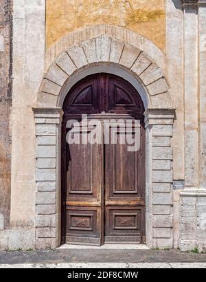 Braun und Ocher. Eine einfache, aber beeindruckende Bogentür aus massivem Naturholz. Details eines alten Vintage-Hauses in Rom, Italien. Stockfoto