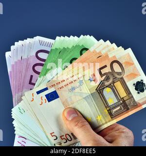 Eine Mann Hand zeigt 20,000 Euro in 100 Euro und 500 Euro Banknoten auf blauem Hintergrund. Kaufen Sie ein neues Auto Stockfoto