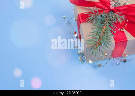 Geschenkschachtel mit roter Schleife und Weihnachtsbaum-Zweig auf festlichem blauen Hintergrund mit Bokeh-Leuchten um und Copyspace für Ihren Text. Flache Lay-Optik. Neu Stockfoto
