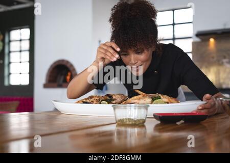 Weibliche afroamerikanische Köchin, die Salz über gerösteten Fisch hinzufügt Teller in der Restaurantküche Stockfoto